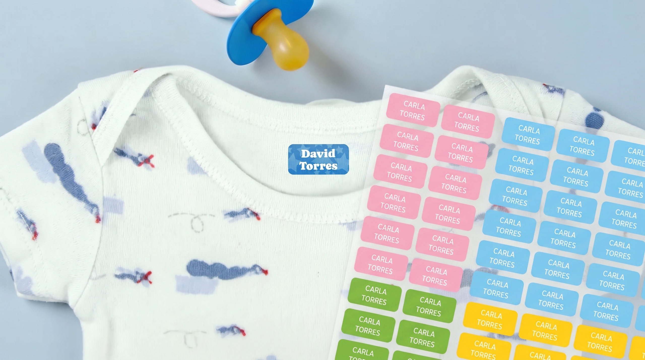 Body de bebé con una etiqueta termoadhesiva con el nombre colocada en el cuello interior, junto a una hoja de etiquetas personalizadas