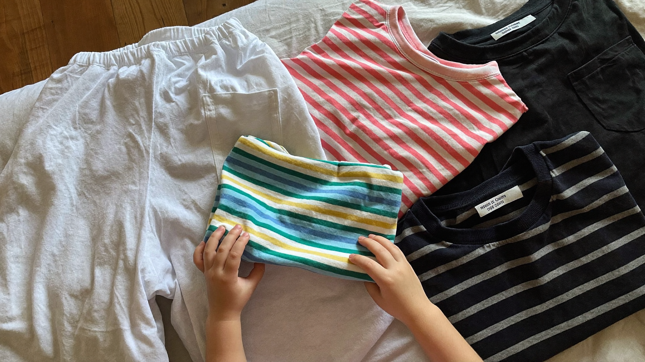 Montones de ropa de niños agrupada por color sobre una cama antes de lavar