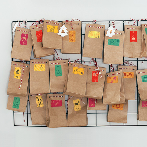 Bolsas de papel kraft colgadas en una rejilla metálica con pegatinas rectangulares numeradas de motivos navideños