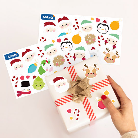 Mano pegando pegatinas de personajes navideños en un regalo envuelto