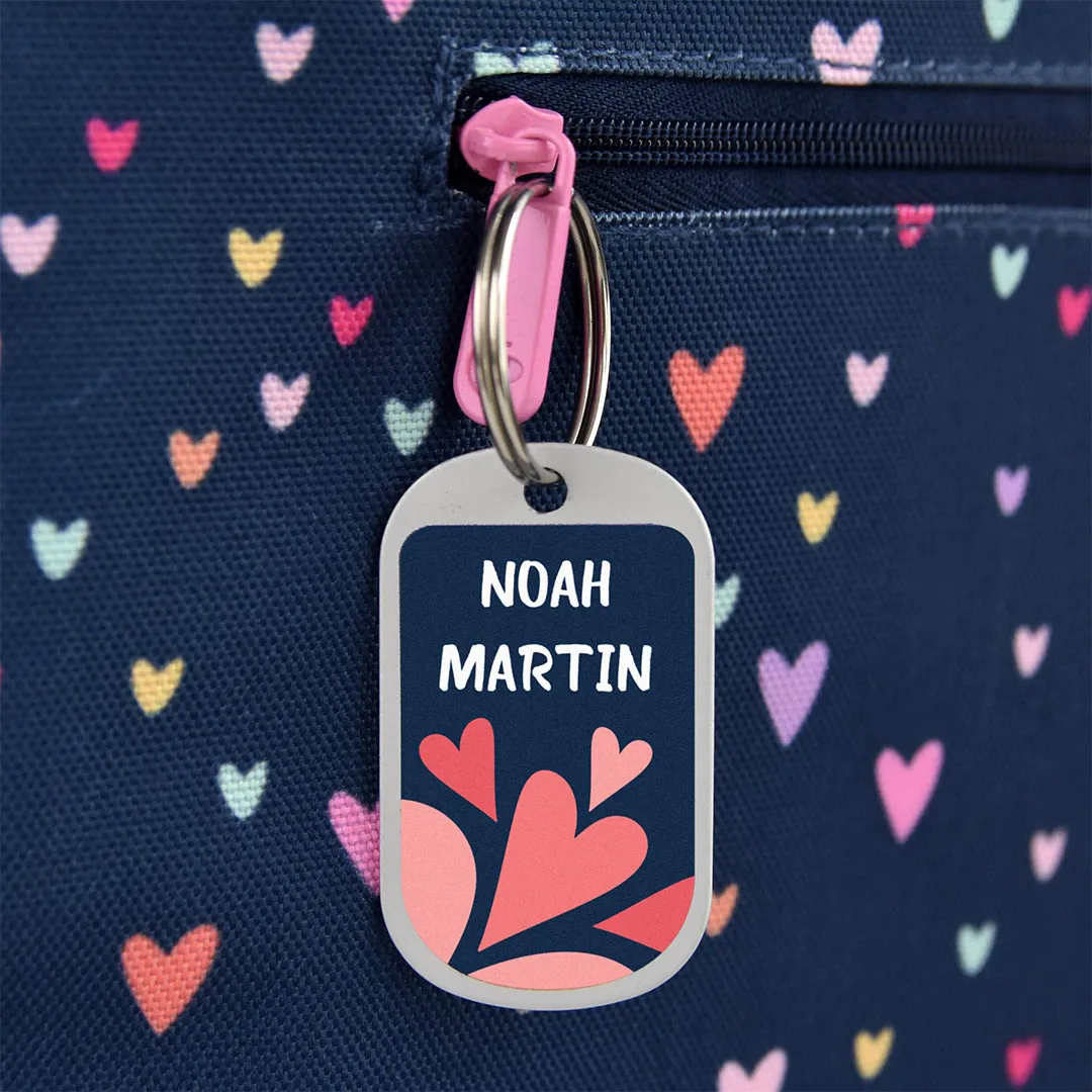 Chapa personalizada con nombre colgada de la cremallera de un tote bag azul marino con corazones