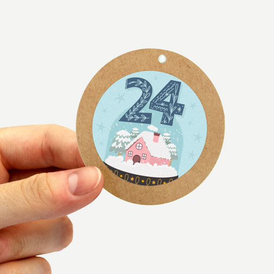 Mano sosteniendo una etiqueta redonda de papel kraft con la pegatina del número 24 del calendario de Adviento