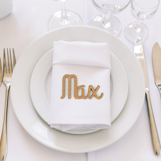 Nombre de madera pequeño con el nombre Max como marcasitio sobre una servilleta blanca en un plato