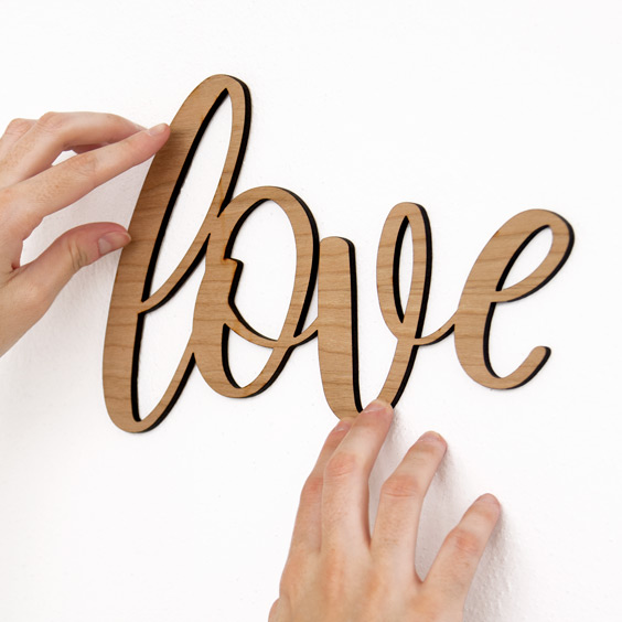 Nombre de madera grande Stikets con la palabra love pegado en una pared blanca