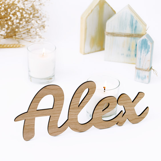 Nombre de madera grande con el nombre Alex apoyado sobre un mueble junto a unas velas