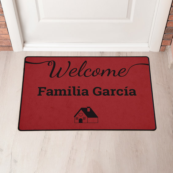 Felpudo personalizado rojo con el motivo de una casa y dos líneas de texto delante de una puerta blanca