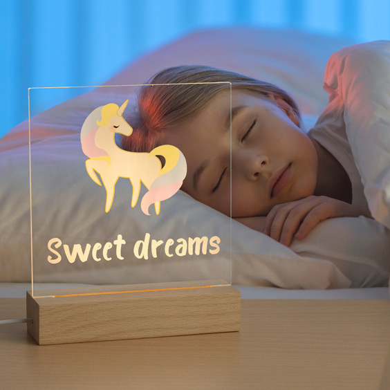 Niña dormida junto a una lámpara LED personalizada encendida con un unicornio en la mesita de noche