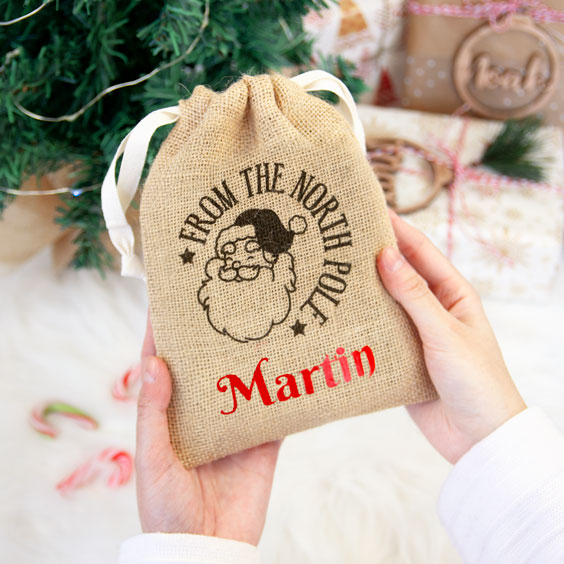 Manos sosteniendo un saco pequeño de yute de Papá Noel personalizado con nombre