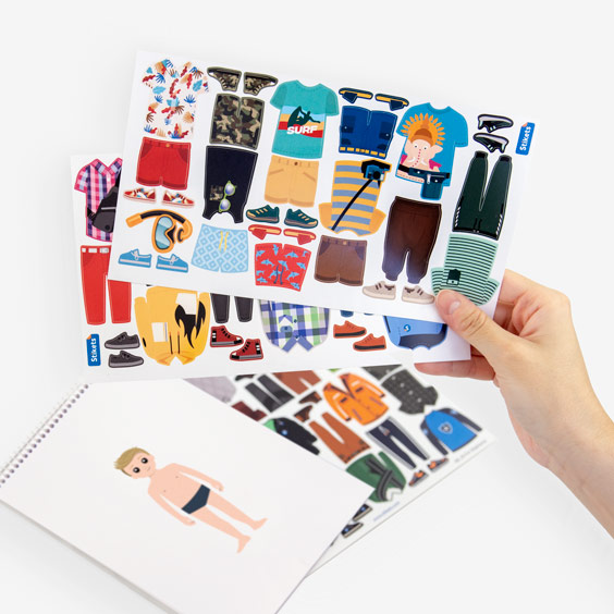 Láminas de pegatinas de ropa para vestir al Twinie junto a una libreta con el avatar del niño