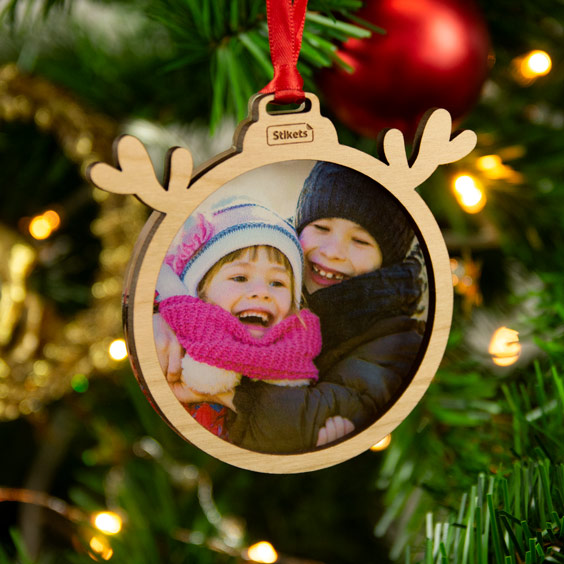 Bola de Navidad con foto de dos niños y marco de madera con astas de reno colgada en el árbol