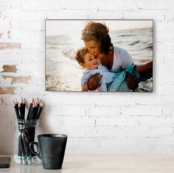 Portafoto personalizado de madera con una foto de madre e hijo en la playa colgado en una pared de ladrillo blanco
